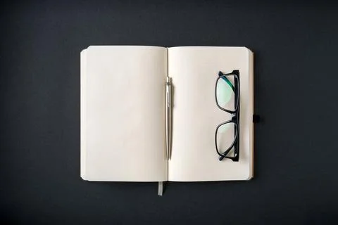 Top view of notebook, glasses and ballpoint pen on dark grey background Stock Photos