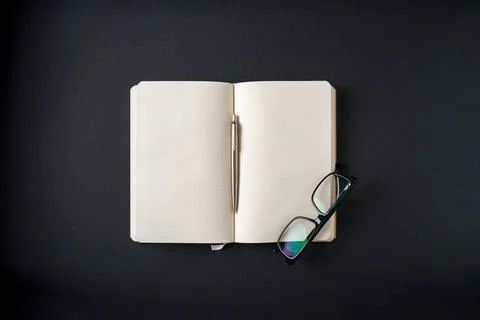 Top view of notebook, glasses and ballpoint pen on dark grey background Stock Photos