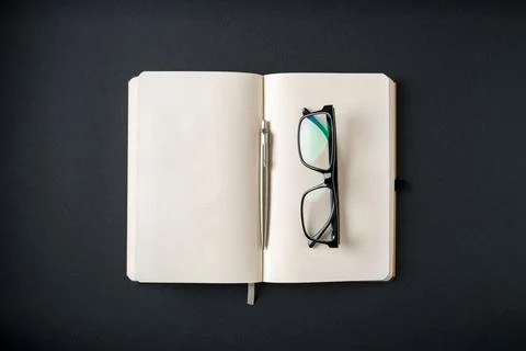 Top view of notebook, glasses and ballpoint pen on dark grey background Stock Photos