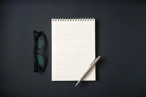 Top view of notebook, glasses and ballpoint pen on dark grey background Stock Photos