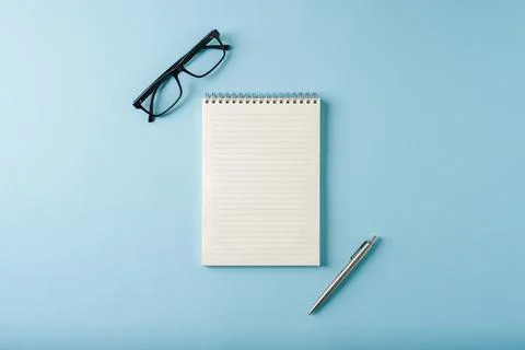 Top view of notebook, glasses and ballpoint pen on blue background Stock Photos