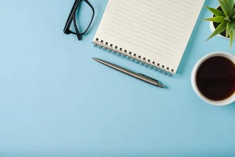 Top view of notebook, glasses, coffee and ballpoint pen on blue background Stock Photos