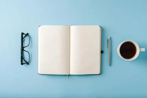 Top view of notebook, glasses, coffee and ballpoint pen on blue background Stock Photos