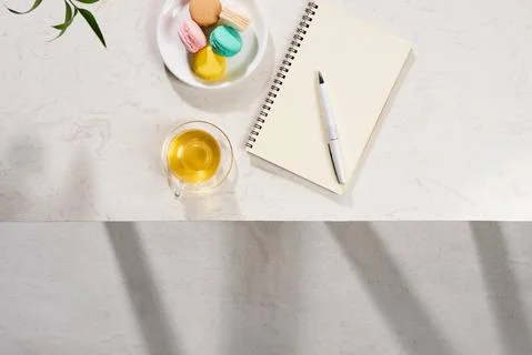 Top view of notebook, pen, cake macaron and tea mug on white background. Flat Stock-Fotos