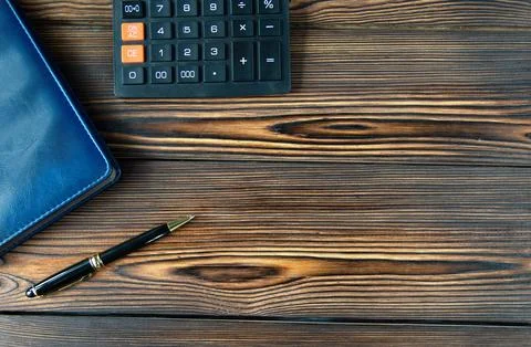 Top view of notepad, calculator, pen. Brown wooden background. Place for reco Stock Photos
