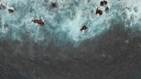 Top view of ocean waves breaking over rocks with white foam patterns Video stock 335987769