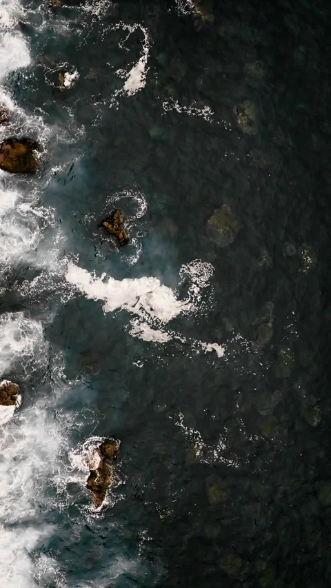 Top view of ocean waves breaking over rocks with white foam patterns Video stock 337308214