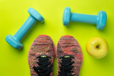 Top view of one apple , two sneakers and two dumbbells on green background.Fi Stock Photos