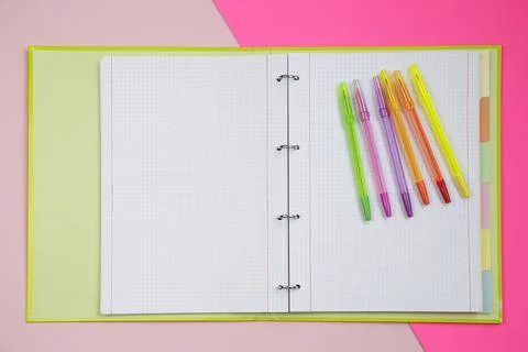 Top view of an open folder with several colorful pens against pink background Stock Photos