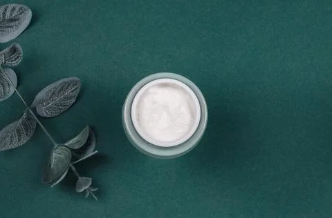 Top view of an open jar of cream and green leaves on a colored background Stock Photos