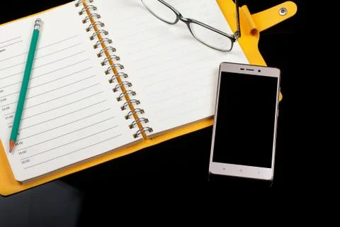 Top view of an open note book, glasses, pen and smartphone on a black background 스톡 사진