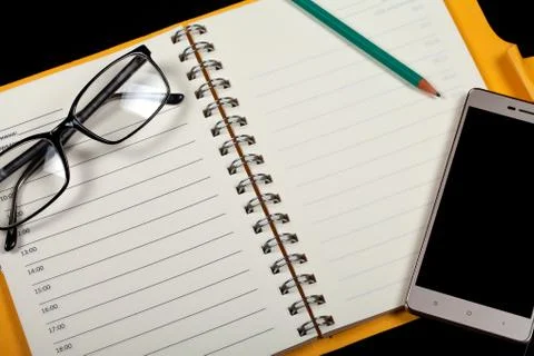 Top view of an open note book, glasses, pen and smartphone on a black background Fotos Stock
