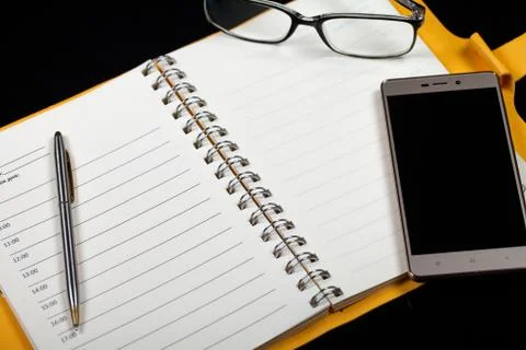 Top view of an open note book, glasses, pen and smartphone on a black background Photos