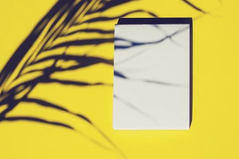 Top view of an open notebook and shadow from palm tree leaf on yellow background Stock Photos