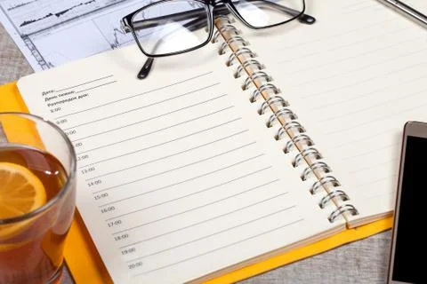 Top view of open notebook, glasses, a cup of tea, pen and smartphone on a w.. Photos