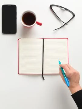 Top view of an open red notebook, a female hand holding a blue pen, a red cup Stock Photos