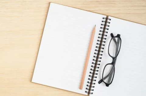 Top view of open spiral notebook with brown pencil and black eye glasses on w Stock Photos