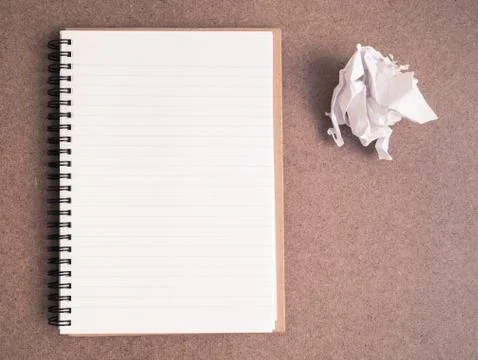 Top view of open spiral notebook with crumpled paper ball on brown background Stock Photos