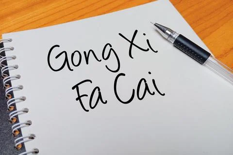 Top view of an open spiral notebook with Gong Xi Fa Cai handwritten text ov.. Stock Photos