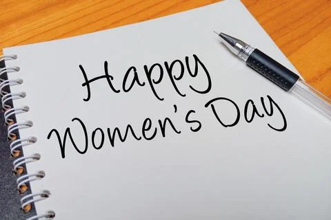Top view of an open spiral notebook with Happy Women's Day handwritten text.. Stock Photos