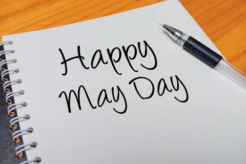 Top view of an open spiral notebook with Happy May Day handwritten text ove.. Stock Photos