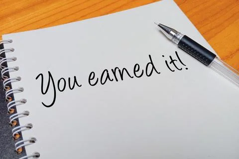 Top view of an open spiral notebook with You earned it! handwritten text ov.. Stock Photos