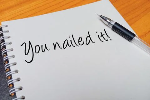 Top view of an open spiral notebook with You nailed it! handwritten text ov.. Stock Photos