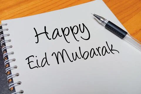 Top view of an open spiral notebook with Happy Eid Mubarak handwritten text.. Stock Photos