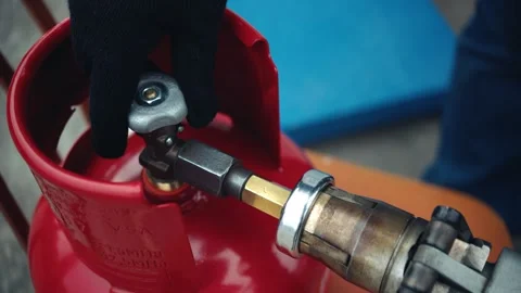 Top view of opening the valve of a red cylinder with a gas pistol attached Stock Footage 282670961
