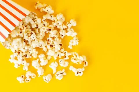 A top view package with popcorn spread all over the yellow background movie.. Stock Photos