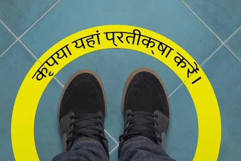 Top view of a pair of feet on a "please wait here" sign in hindi. Concept of  Stock Photos