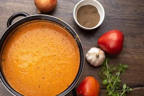 Top view of a pan with tomato puree soup and ingredients on a wooden backgrou Stock Photos