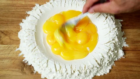 Top view of pasta making: perfect egg yolks are beaten inside a well of Stock Footage 157581670