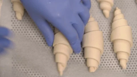 A top view of a pastry chefs hands placing raw croissants onto a baking tray in Stock Footage 106377956