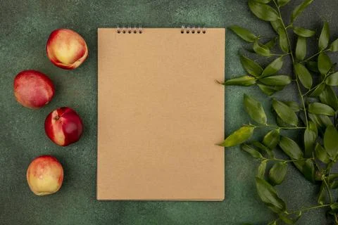 Top view of pattern of peaches with note pad and leaves on green background.. Stock Photos