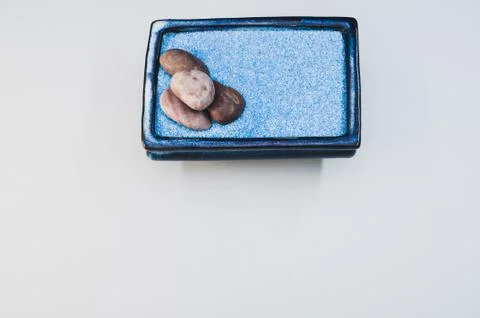 A top view of pebbles on a rectangular box filled with small blue rocks on wh 스톡 사진