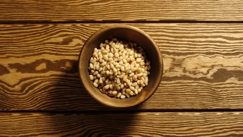 TOP VIEW: Peeled pine nuts appear in wooden cup and full this cup - Stop motion Stock Footage 96799642