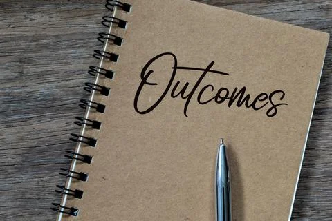 Top view of pen and notebook written with text OUTCOMES. Stock Photos
