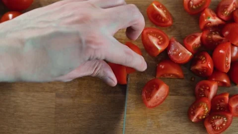 Top view person cuts cherry tomatoes on a wooden cutting board in a kitchen. The Stockbeeldmateriaal 338290637