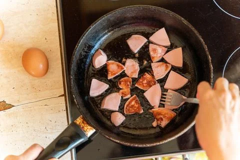 Top view of a person frying triangular slices of sausage in a black pan on a  Stock Photos