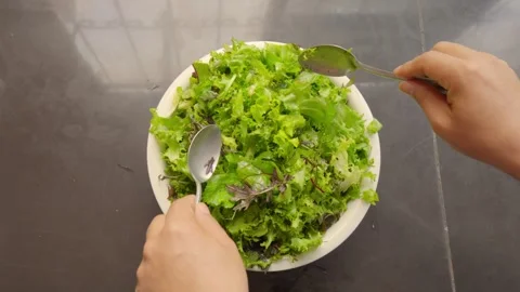 Top view of person hands mixing fresh green salad with spoons in bowl Stockbeeldmateriaal 338144537