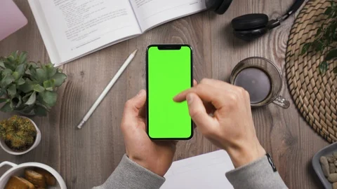Top view. Phone in hands, swipe up on green screen. Chroma key. Workplace table. 動画素材 129307528