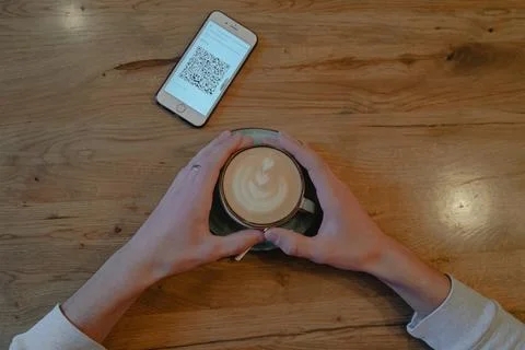 Top view of phone with kuar code and hands holding a cup of coffee in a cafe Foto stock