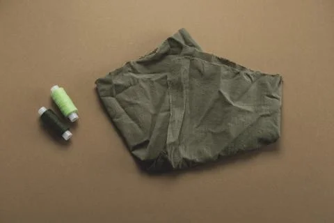 Top view of a piece of fabric and a spool of thread on a brown background Stock Photos