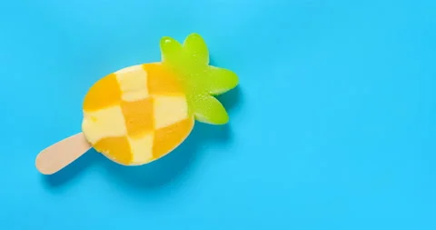 Top view pineapple shape popsicle melting timelapse on blue background at 8k Stock Footage 135289344