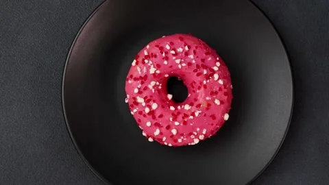 Top view of a Pink glazed Doughnut with colorful sprinkles on a black plate Video stock 237300688