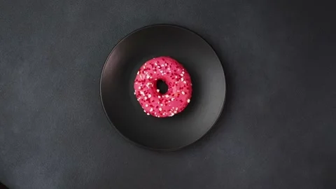 Top view of a Pink glazed Doughnut with colorful sprinkles on a black plate Stock Footage 237300695