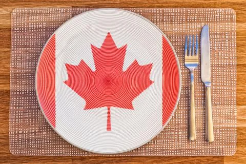 Top view of a plate with the flag of Canada and silverware on a wooden table. Stock Illustration