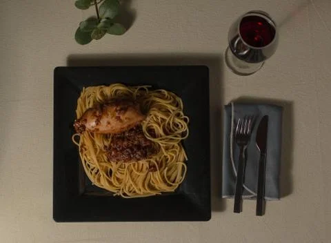Top view of a plate with stuffed squid and noodles next to a glass of red win 스톡 사진