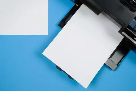 Top view of the printer and a blank sheet of a4 paper on a blue background. Stock Photos
